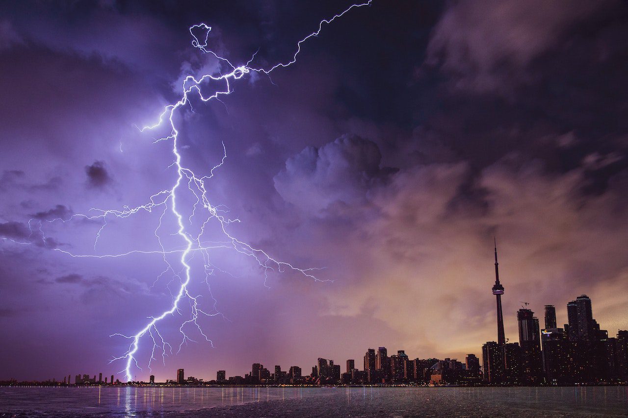 Lightning bolt striking water near a city at night, symbolizing the power and intensity of electrical energy, with Laswell Electric offering reliable lightning protection services.